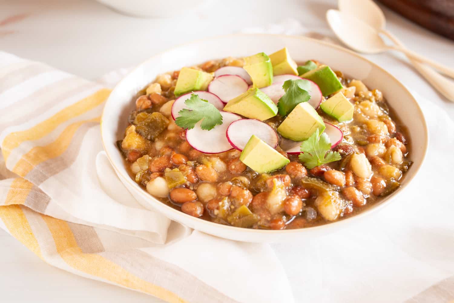 bowl of vegan tomatillo stew with beans, hominy, radishes, and avocado