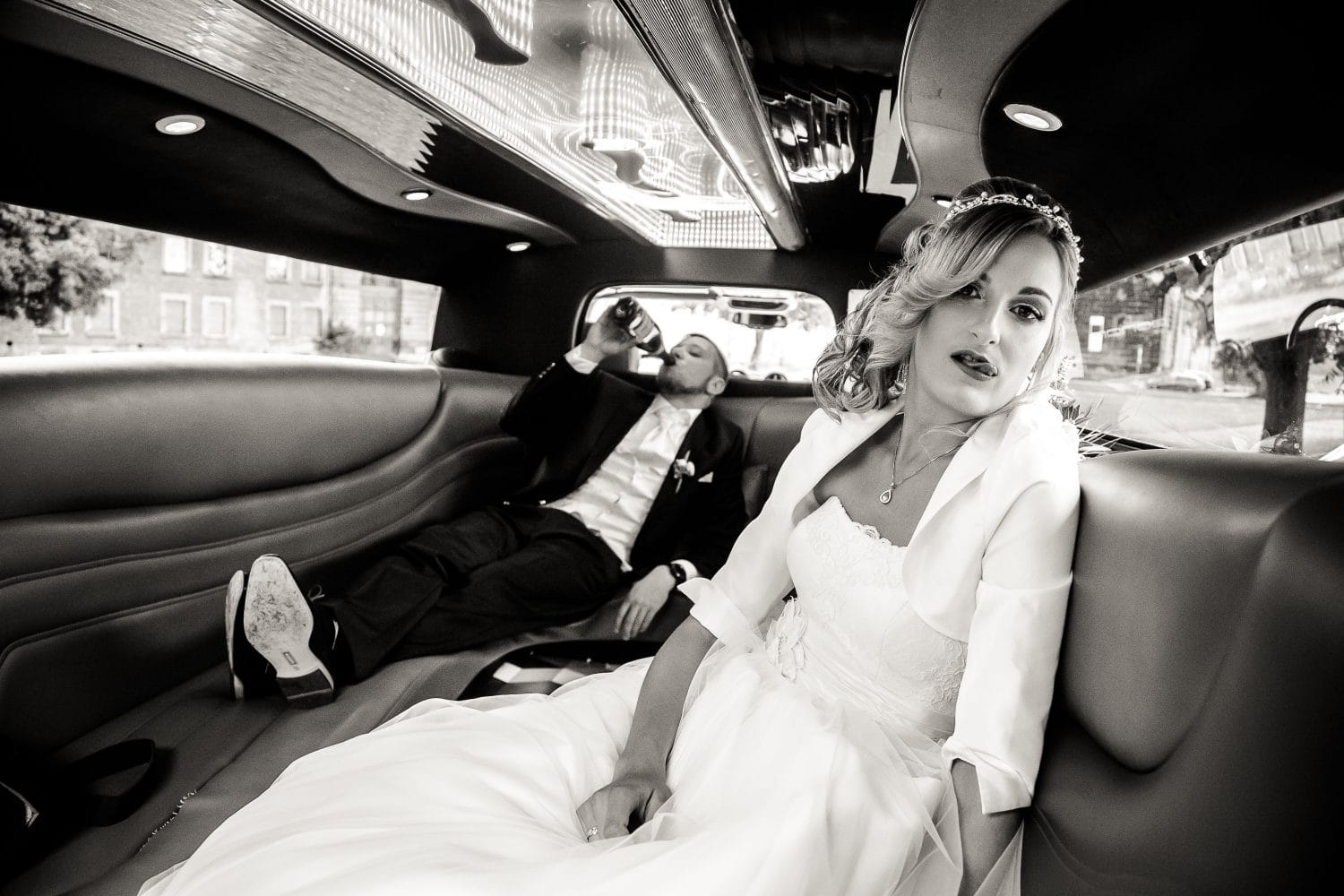 Sie hat "Ja" gesagt, er hat Durst: die Braut im Hochzeitskleid posiert schick in der Limo, während der Bräutigam im Anzug hinten lässig aus der Flasche Champus trinkt. Prioritäten im Hochzeitsauto klar verteilt – Glamour vorne, Chillen (mit Getränk) hinten. Canon 6d & EF 24-105 f4.0