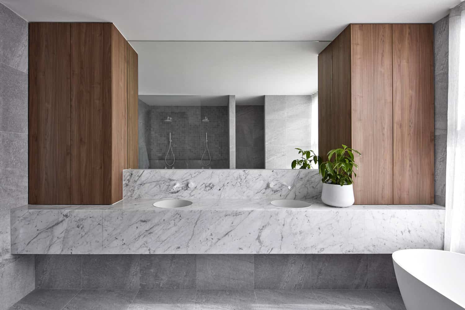 Floating marble vanity with dual sinks, flanked by timber cabinets, set against grey stone wall tiles.