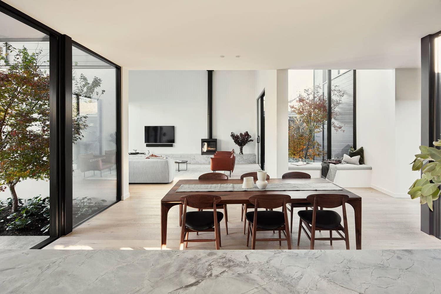 Modern dining room with dark timber table, flanked by glass courtyard doors and open-plan living area beyond.