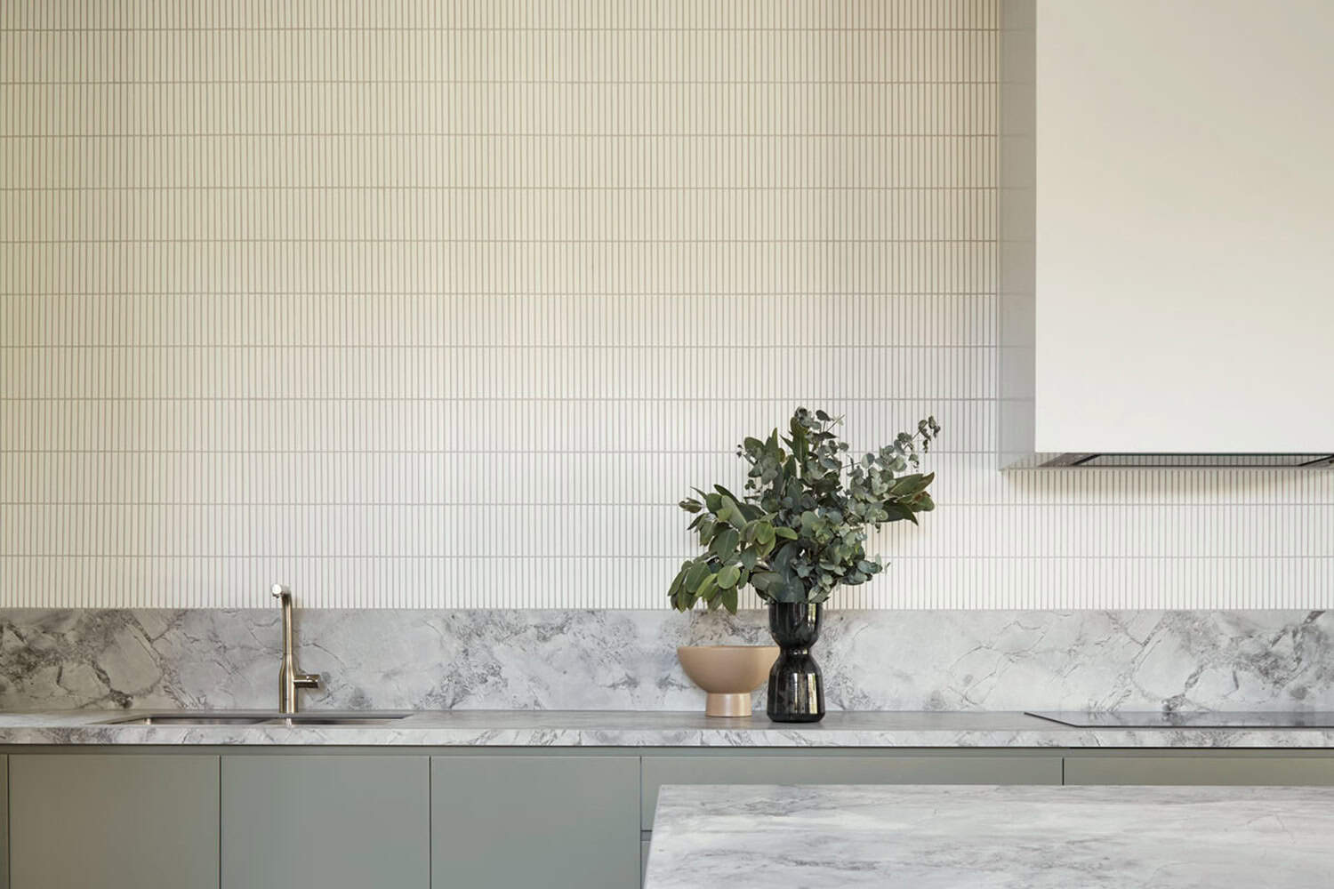 Kitchen splashback with grey marble benchtop, vertical kitkat tiles, brass tapware, and a vase with eucalyptus.