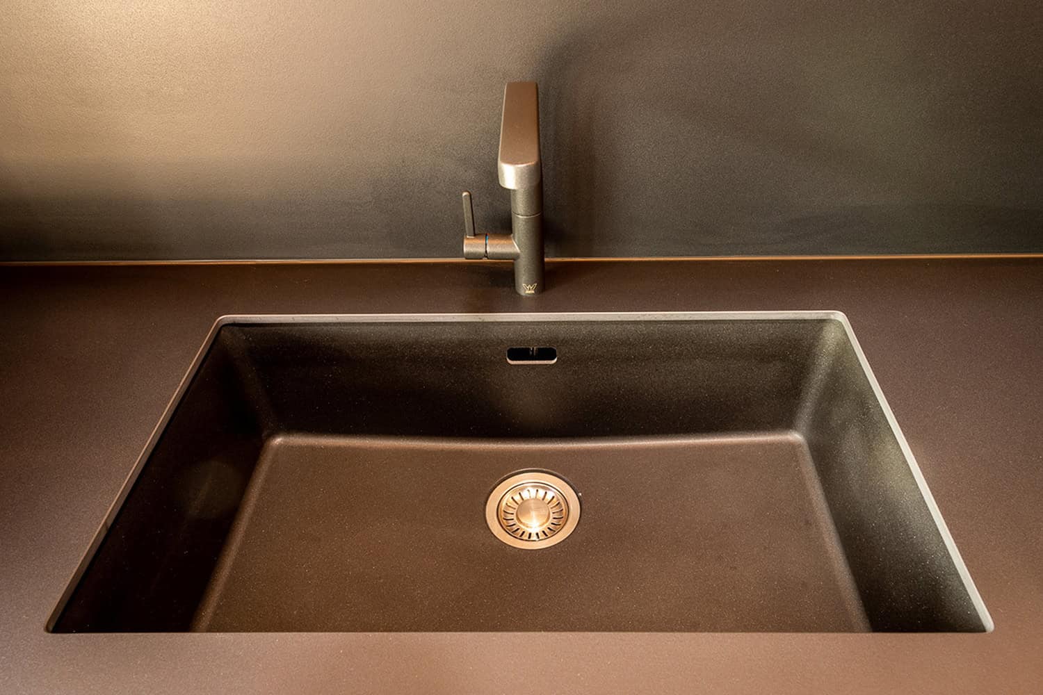 Top-down view of a dark composite undermount sink with matching metallic tapware.