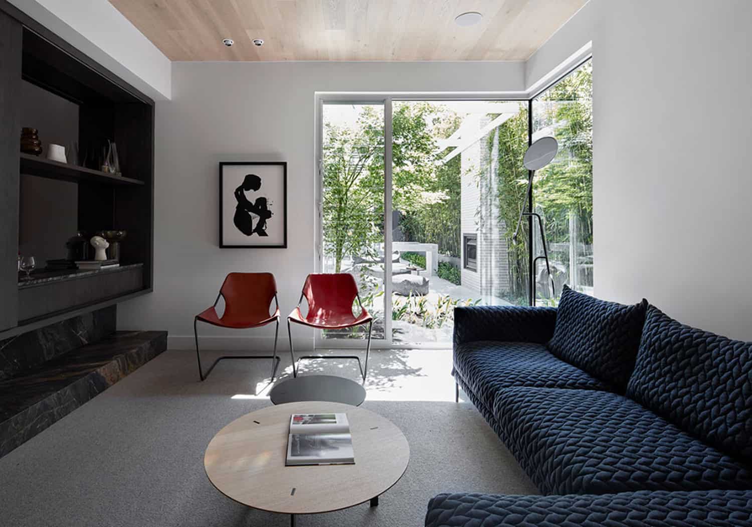 Contemporary sitting room with dark blue textured sofa, red accent chairs, and glass garden doors.