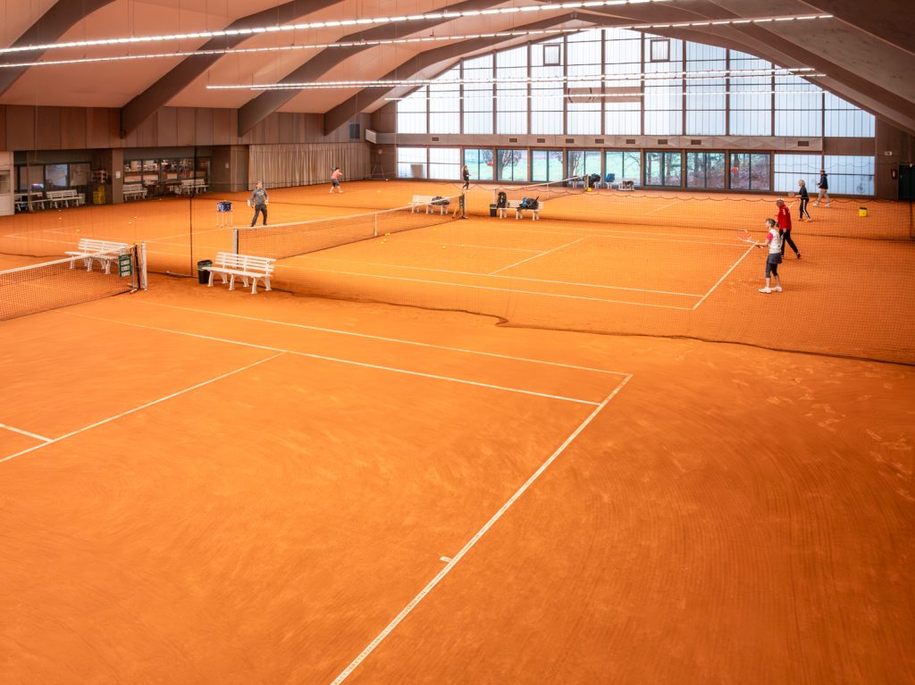 Tennisplatz im modernen Indoor-Sportzentrum, professionell gepflegt und gut beleuchtet.