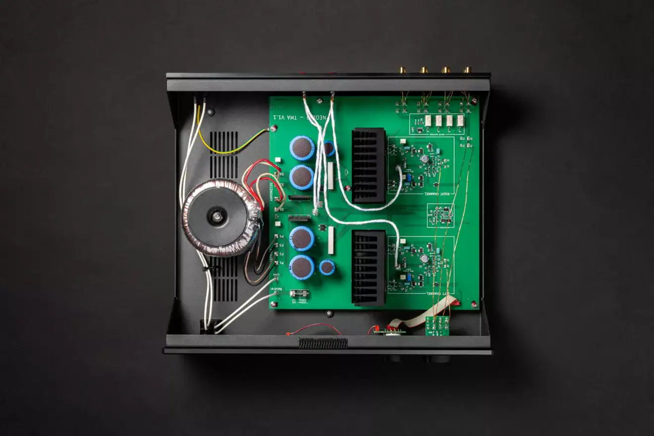 Le Neodio TMA est vu de dessus, capot ouvert, circuits à l'air libre. De gauche à droite l'alimentation toroïdale fabriquée en Espagne, condensateurs, radiateurs passifs et circuits électroniques sur carte verte. Quelques fils traversent la carte