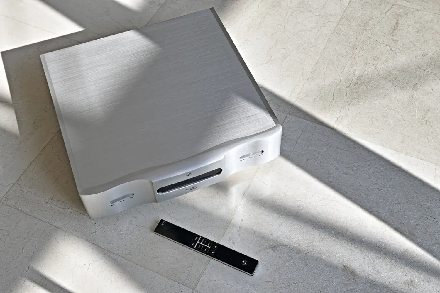 Vermeer Audio Two photo artistique du Two et de sa télécommande posés sur un sol clair