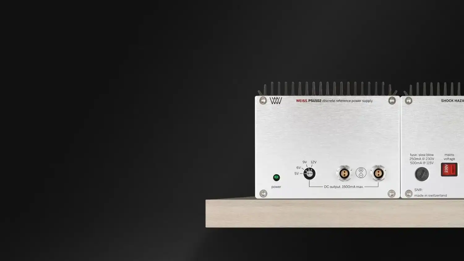 Weiss PSU102 vue artistique avec l'alimentation posée sur une étagère en bois sur fond noir