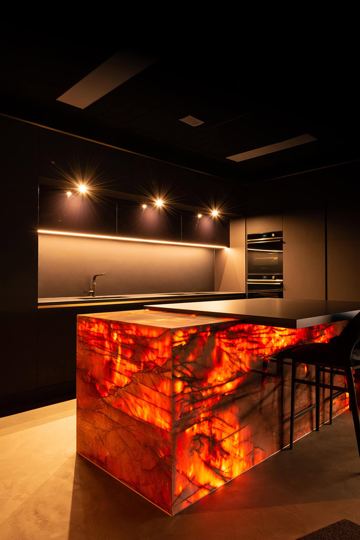 Illuminated amber onyx island bench feature in a moody, dark luxury kitchen.