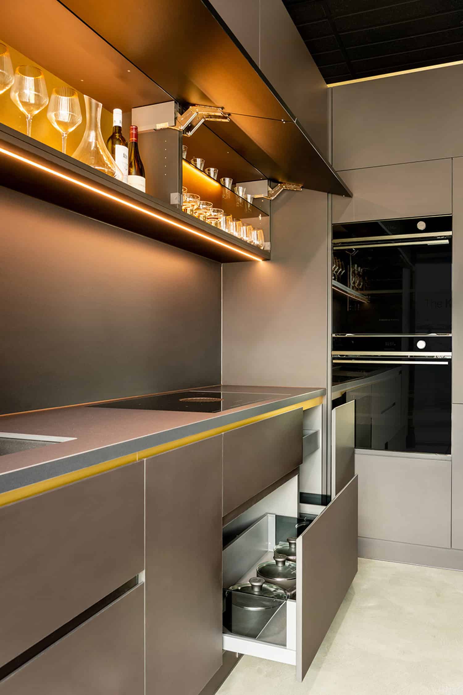 Angled view of a dark modern kitchen with open deep drawers for pots and lift-up glass cabinets.