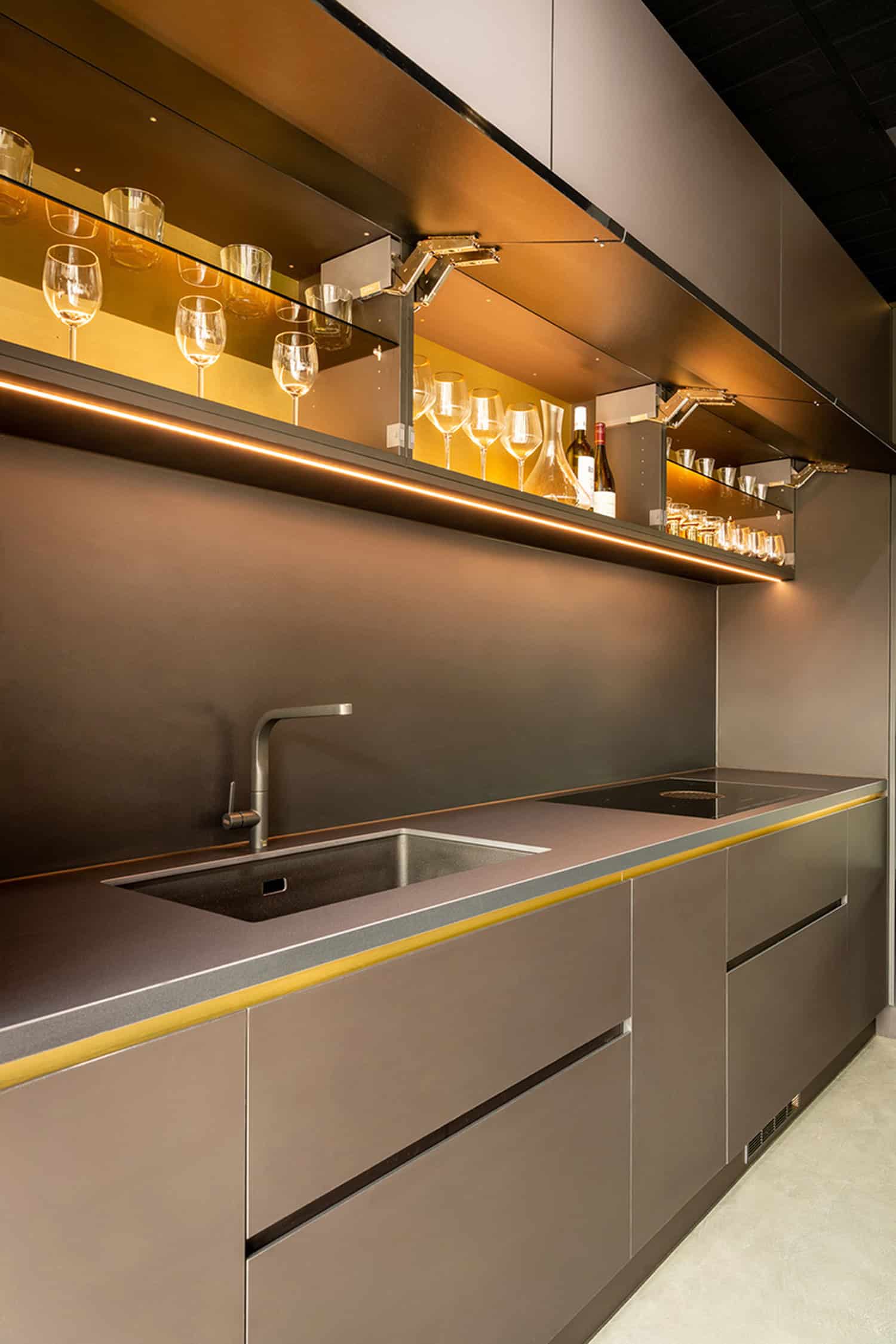 Sleek dark grey kitchen cabinets with warm LED strip lighting and glass shelving.