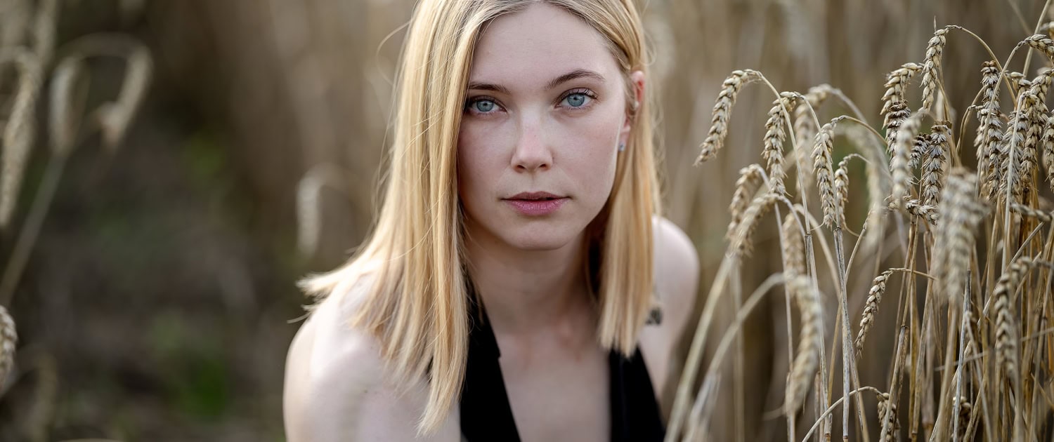 Umgeben von reifem Getreide strahlt eine Frau in diesem natürlichen Porträt eine ruhige und unmittelbare Präsenz aus, mit Tagelicht fotografiert in Bad Langensalza mit der Canon EOs R5II & dem RF 135mm