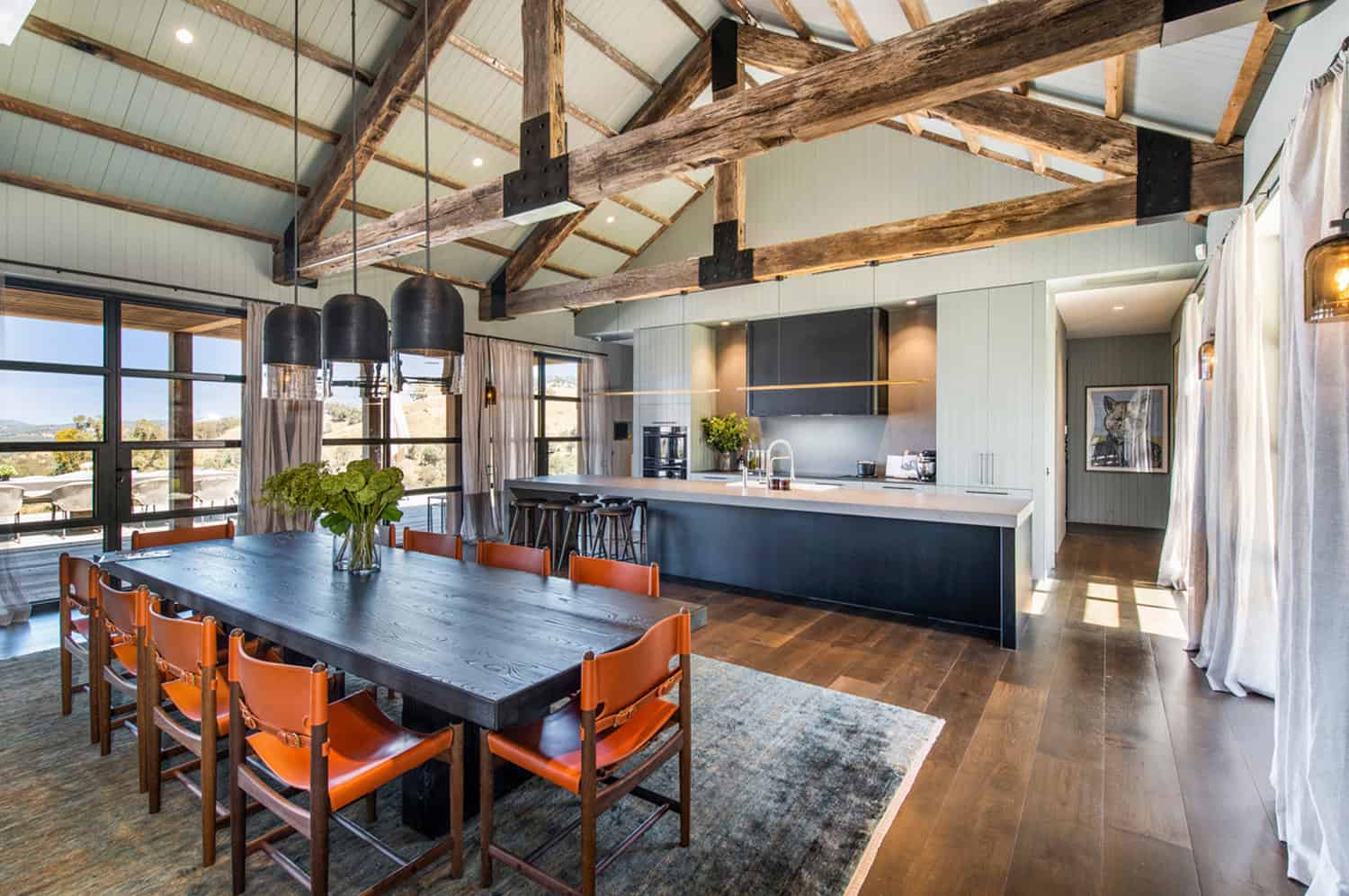 Rustic modern open-plan kitchen and dining area with exposed timber ceiling beams and leather chairs.