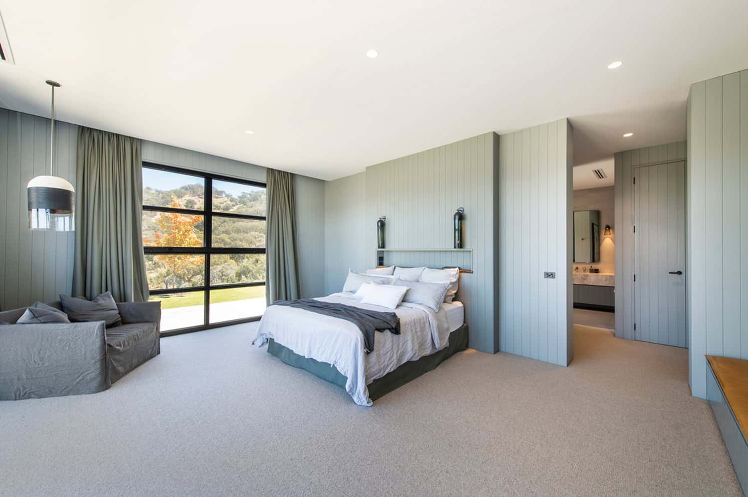 Serene bedroom with sage green paneled walls, a plush bed, large landscape window, and ensuite access.