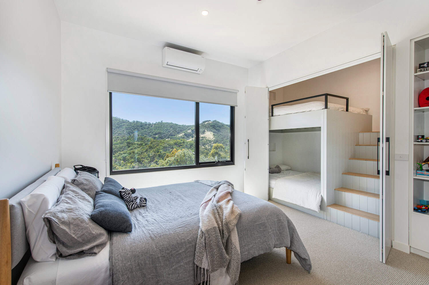 Modern bedroom featuring built-in bunk beds with steps, a double bed, and scenic mountain views.