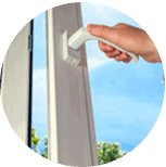 A hand is opening a white window handle with a clear blue sky visible outside.