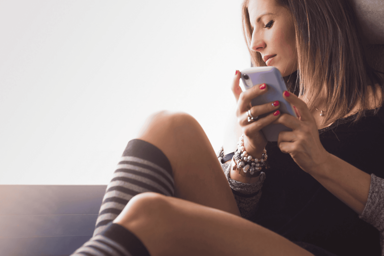 Featured photo of woman holding phone and looking out the window, thinking.
