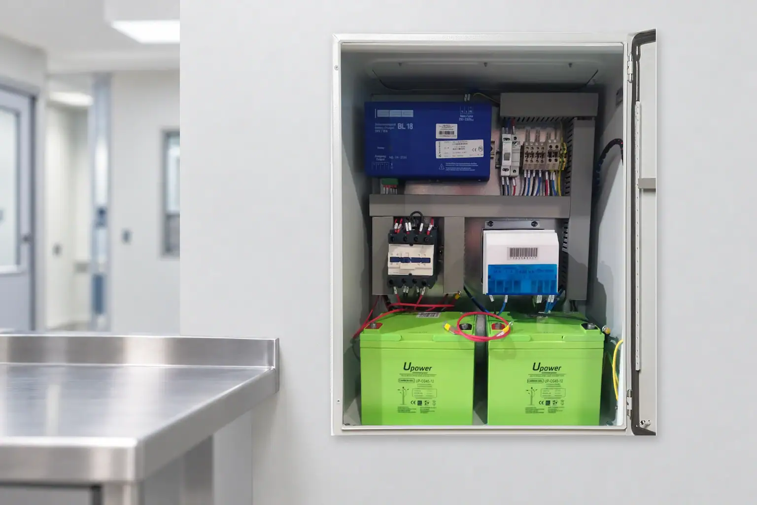 Inside the ETKHO backup unit Interior of an ETKHO backup unit with a charger, connections and two green batteries, in a conceptual technical setting
