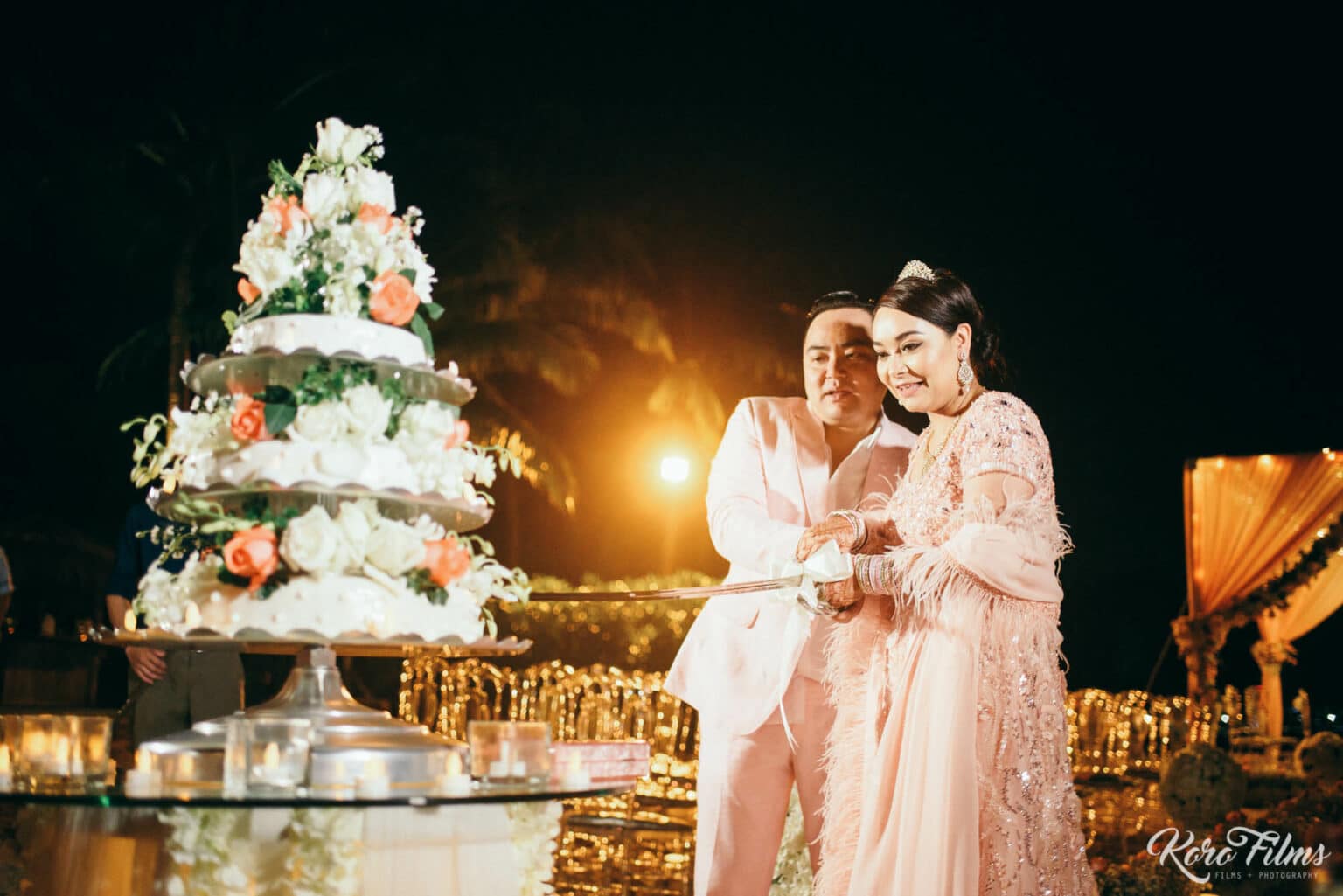Bride and groom in pink and white beside a tall white flower cake at their beach reception in Pattaya
