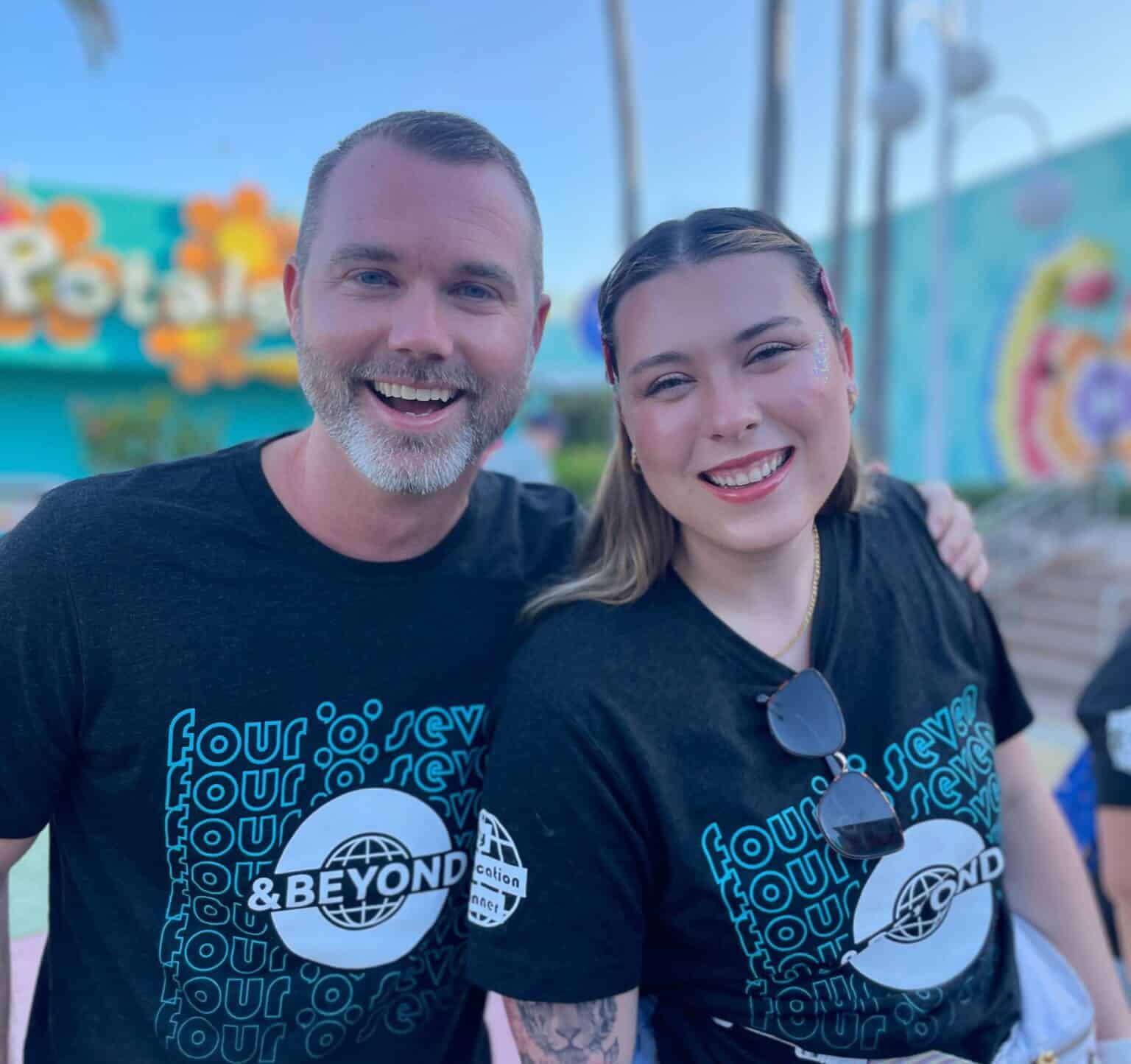 Happy couple at a Florida amusement park celebrating vacation fun, wearing "407 & Beyond Vacation Co." shirts.