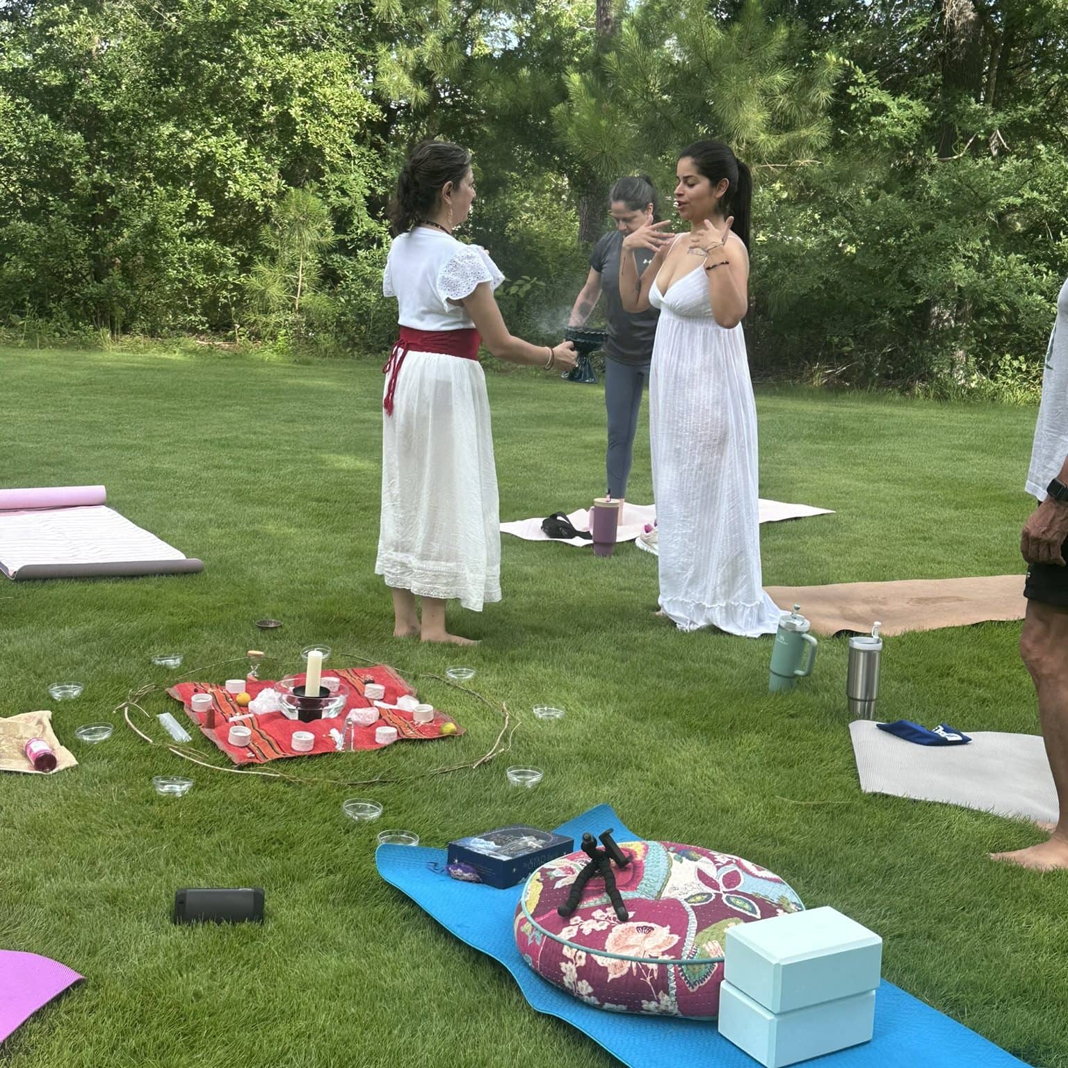 Serene outdoor yoga and wellness session in lush green park, featuring women practicing mindfulness and meditation with yoga mats, candles, and wellness accessories, promoting relaxation and spiritual well-being.