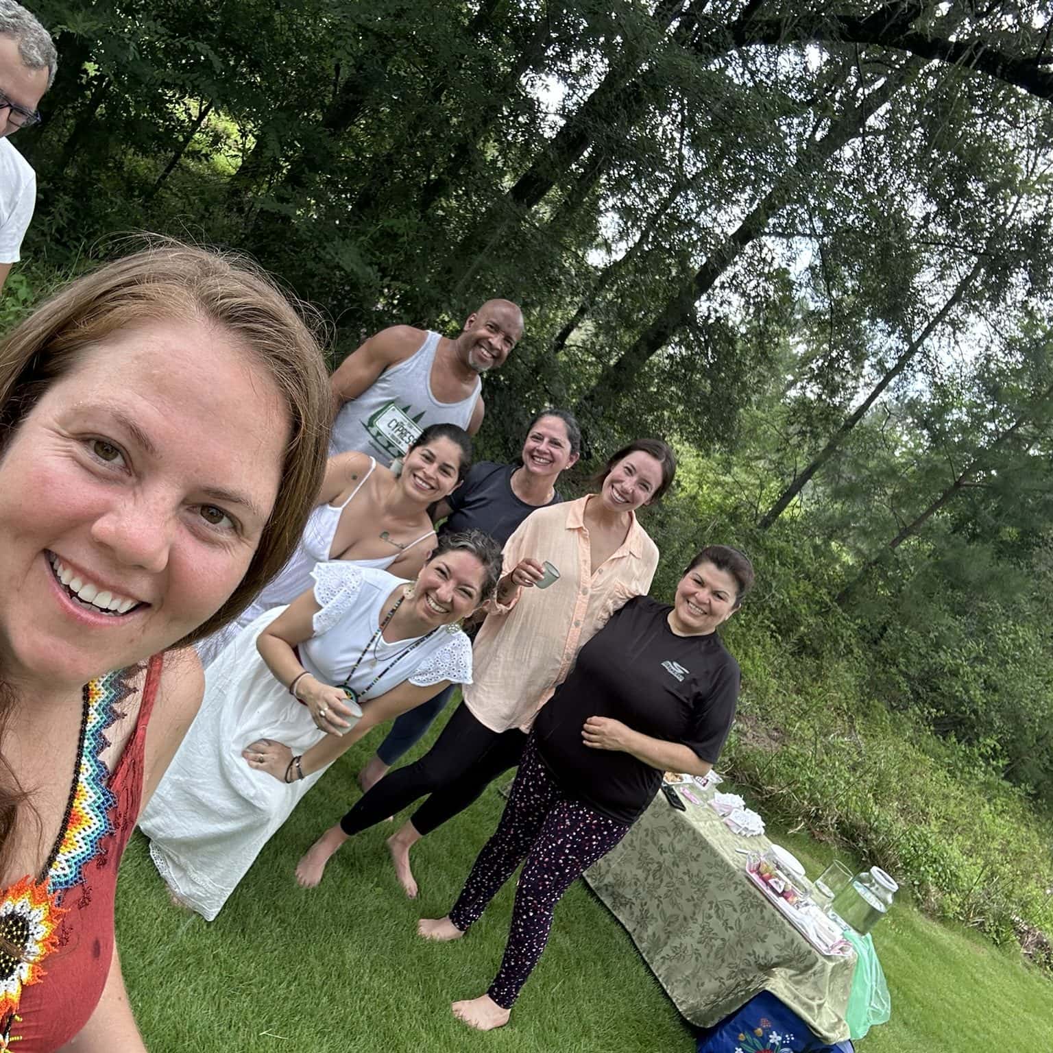 Joyful group of diverse friends enjoying a sunny outdoor gathering at Soulstice Living, celebrating wellness, community, and natural beauty in a lush green setting.