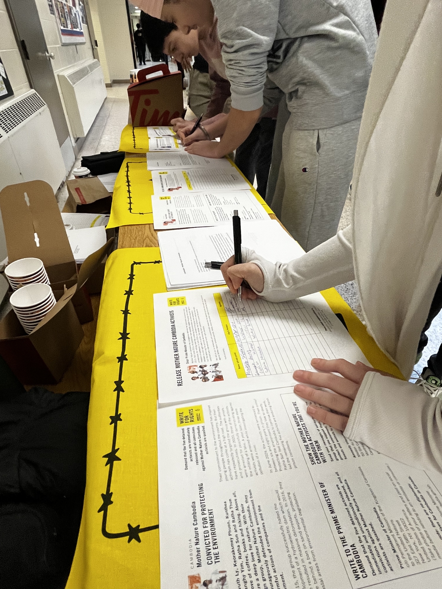 Students writing handwritten messages on Amnesty International Write for Rights letter templates laid out on a table.