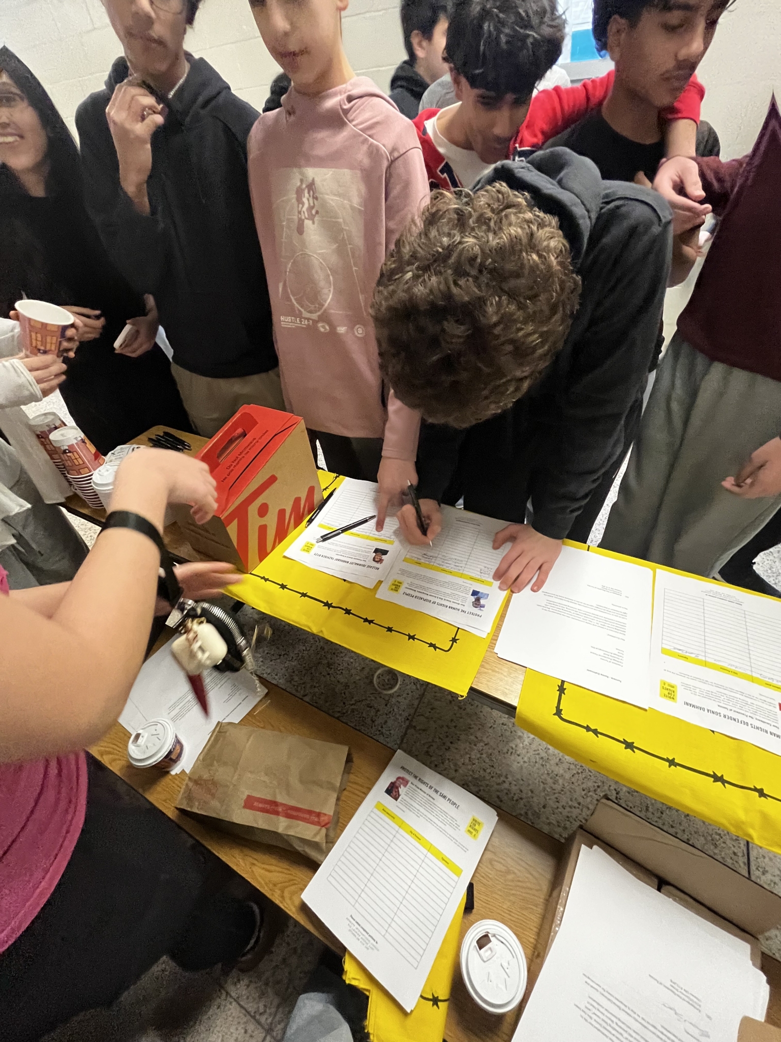 High school students gathered around a table, reading case sheets and signing letters during an Amnesty International Write for Rights school action.