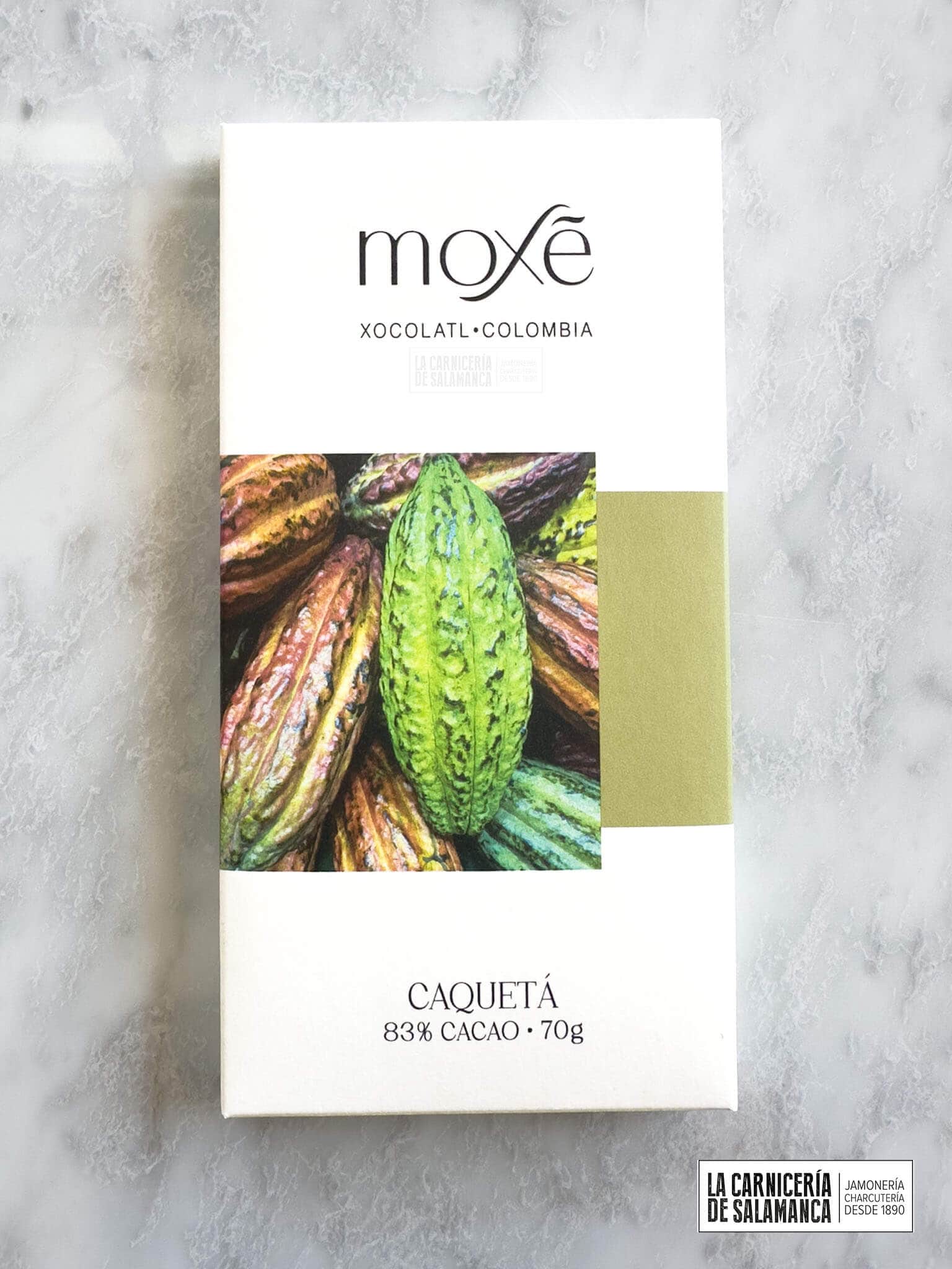 Tableta de chocolate Moxé Caquetá, 83% cacao, presentada en un empaque minimalista con una imagen vibrante de mazorcas de cacao de colores, mostrando la calidad del cacao colombiano. Disponible en la Carnicería de Salamanca.