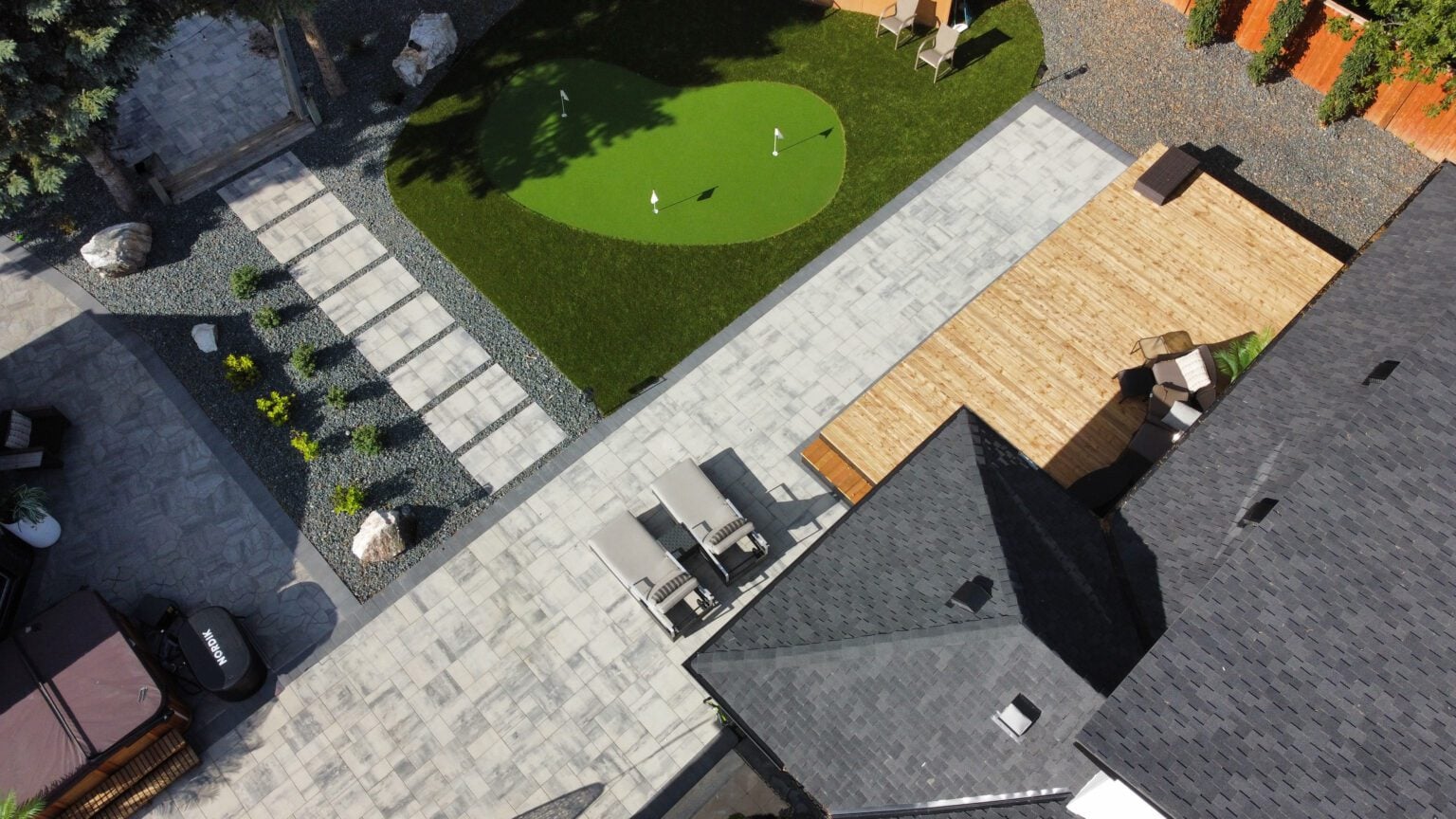Aerial view of backyard with putting green, stone walkway, wooden deck, and patio seating.
