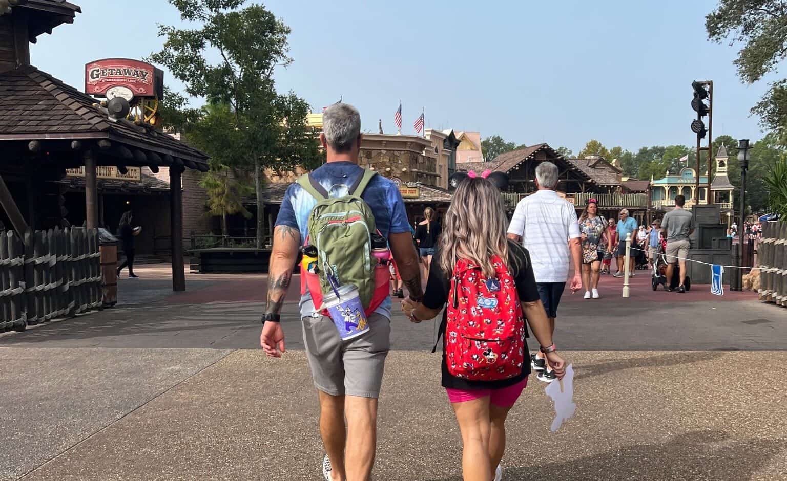 Brightly dressed couple walking hand-in-hand through Disney park, families enjoying attractions, perfect for Orlando vacation planning.