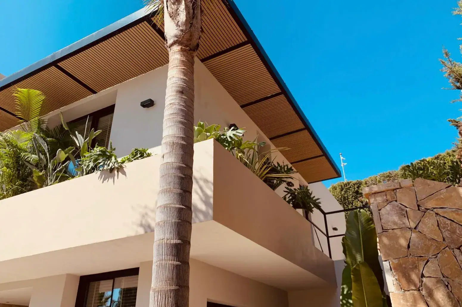 Fachada de villa de lujo con terraza, vegetación tropical y techos revestidos de madera.