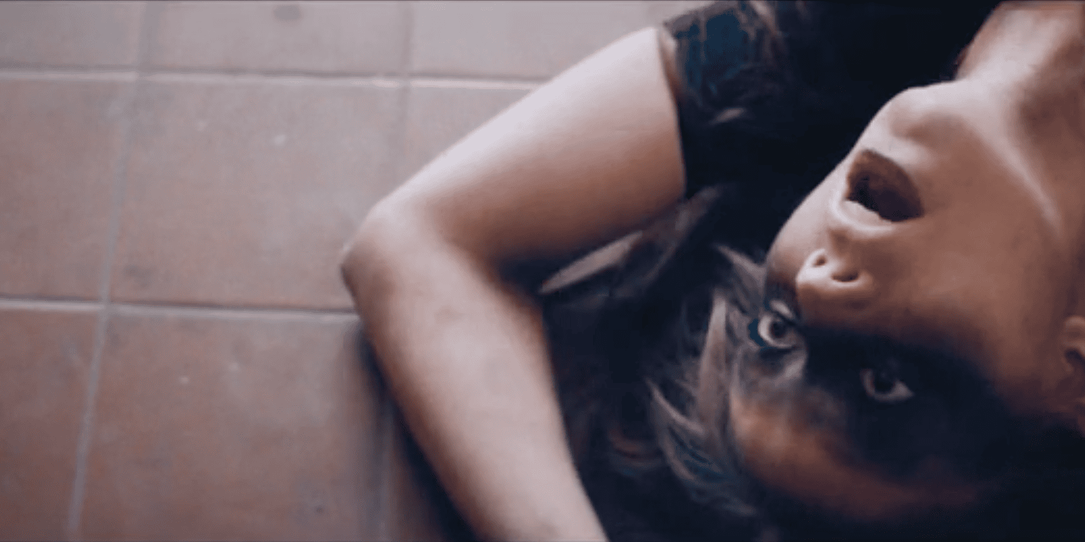 Cinematic music video production still featuring an intense, moody narrative scene with a female artist on a bathroom floor.