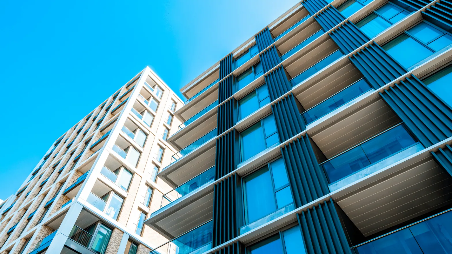 Modern high-rise apartment buildings with glass balconies and vertical panel details against a clear blue sky.