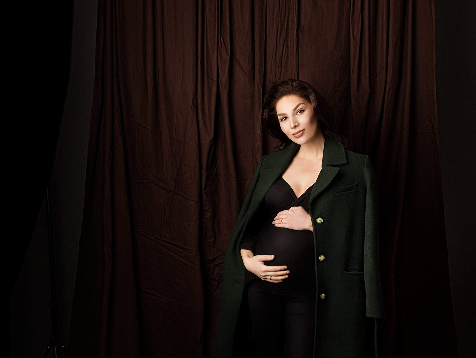 Elegant gravidfotografi av gravid kvinne i mørke klær, lavt lys, studio-innstilling, nært, fokusert på graviditet og kvinnelig skjønn, profesjonell gravidfotografering.