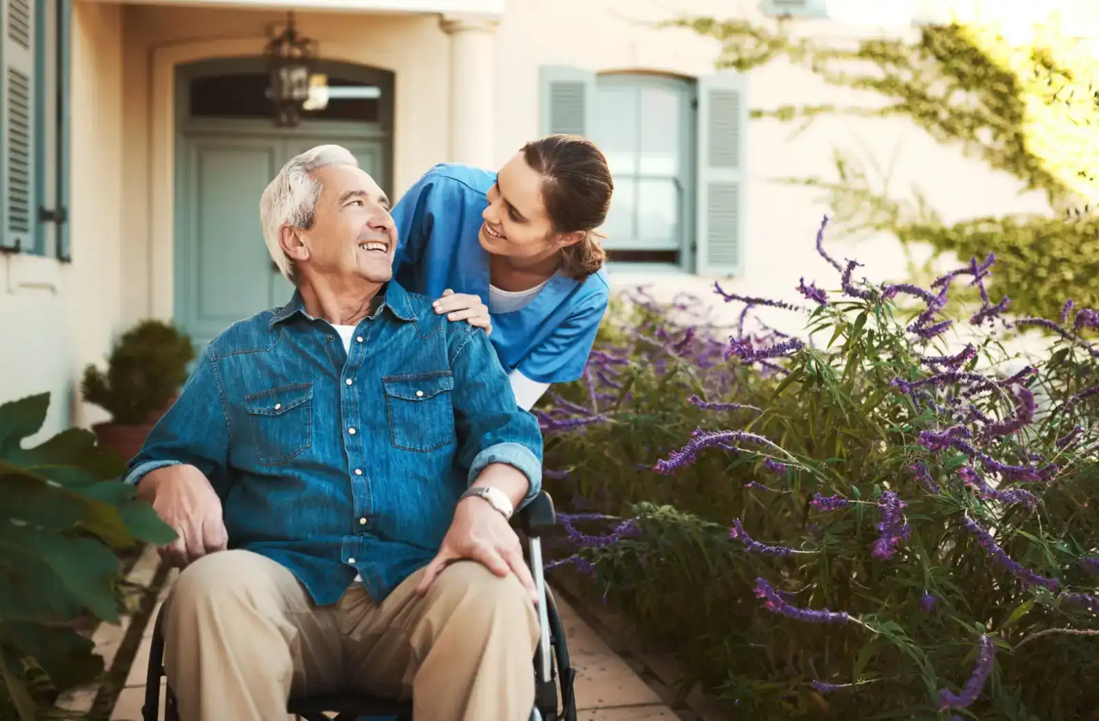 Caregiver assisting an elderly man in a wheelchair outdoors, surrounded by vibrant flowers, showcasing compassion and support in a serene environment.