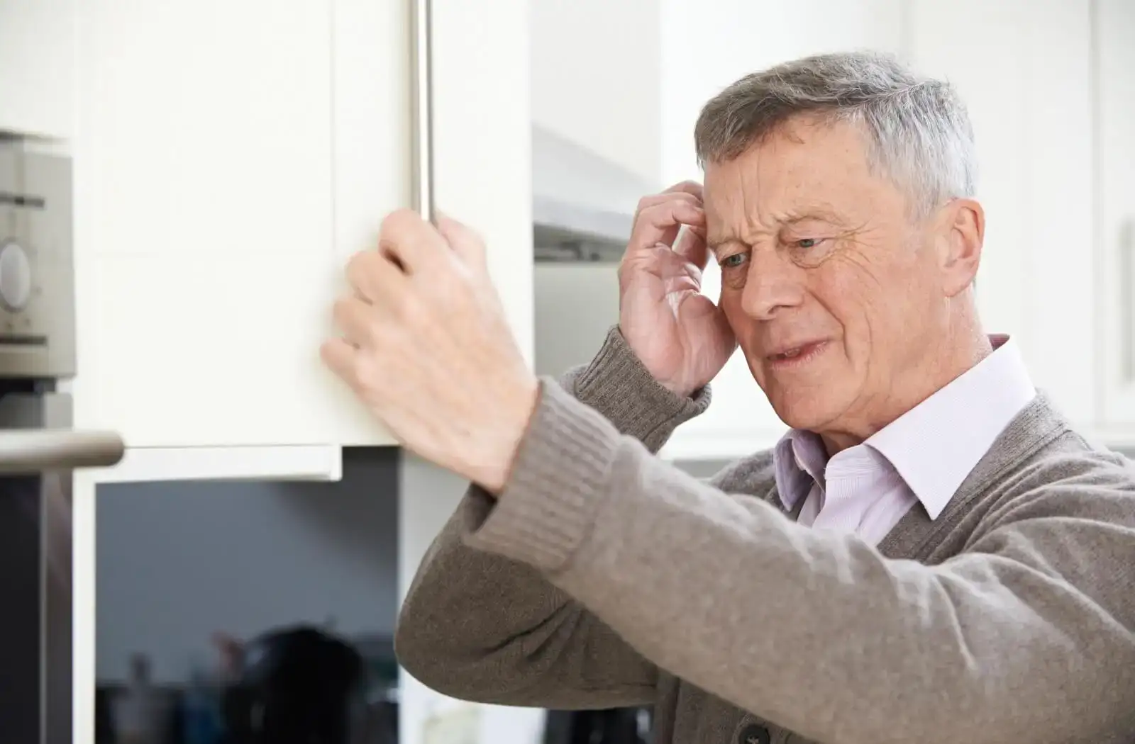 Elderly man looking confused while reaching for a kitchen cabinet, showcasing moments of everyday life and the challenges of aging.
