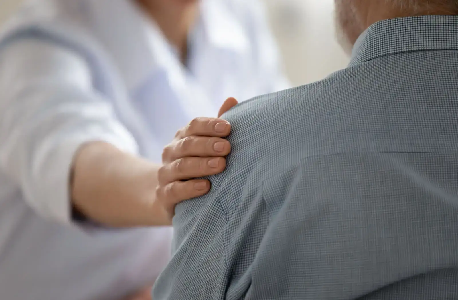 A healthcare professional gently comforting an elderly patient by placing a hand on their shoulder, symbolizing support and care in a medical setting.