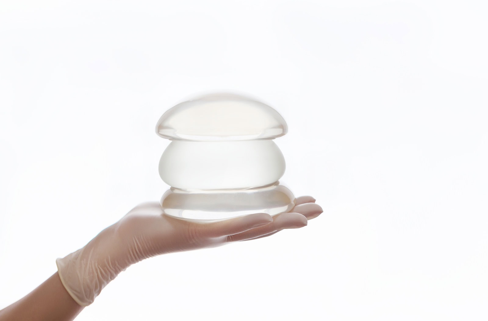Hand holding two silicone breast implants of different sizes while another hand points to select one during consultation