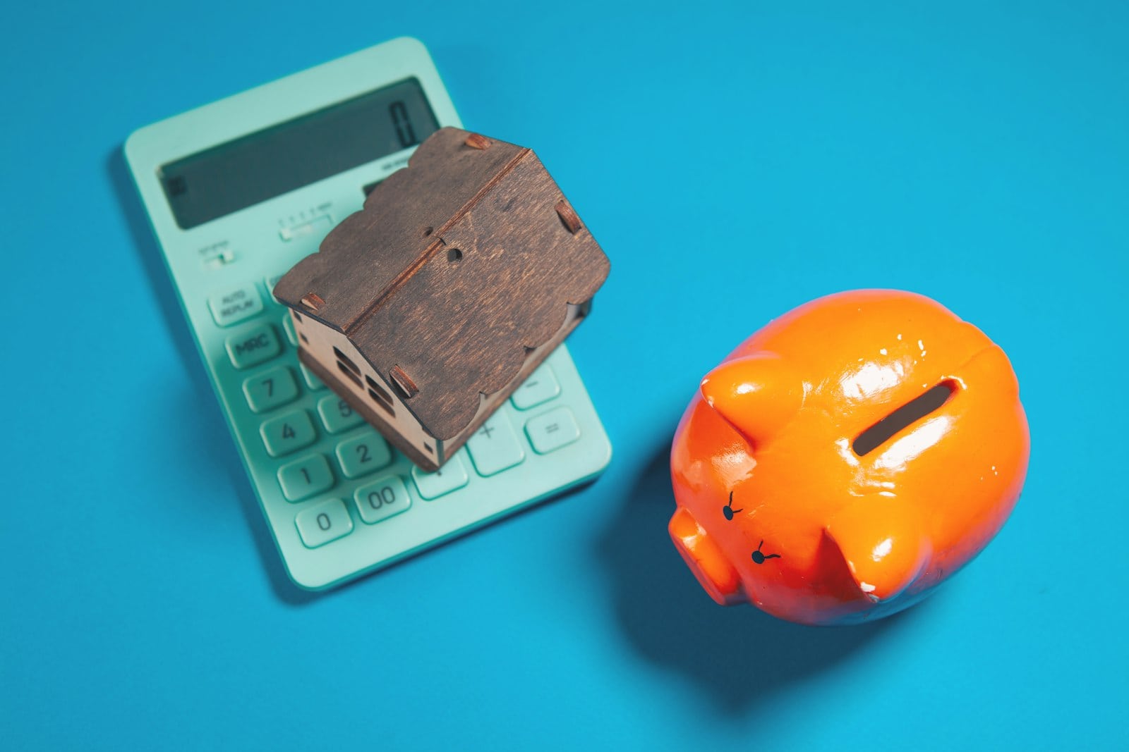 A calculator, piggy bank and small model house, representing the financial cost of spray foam insulation removal