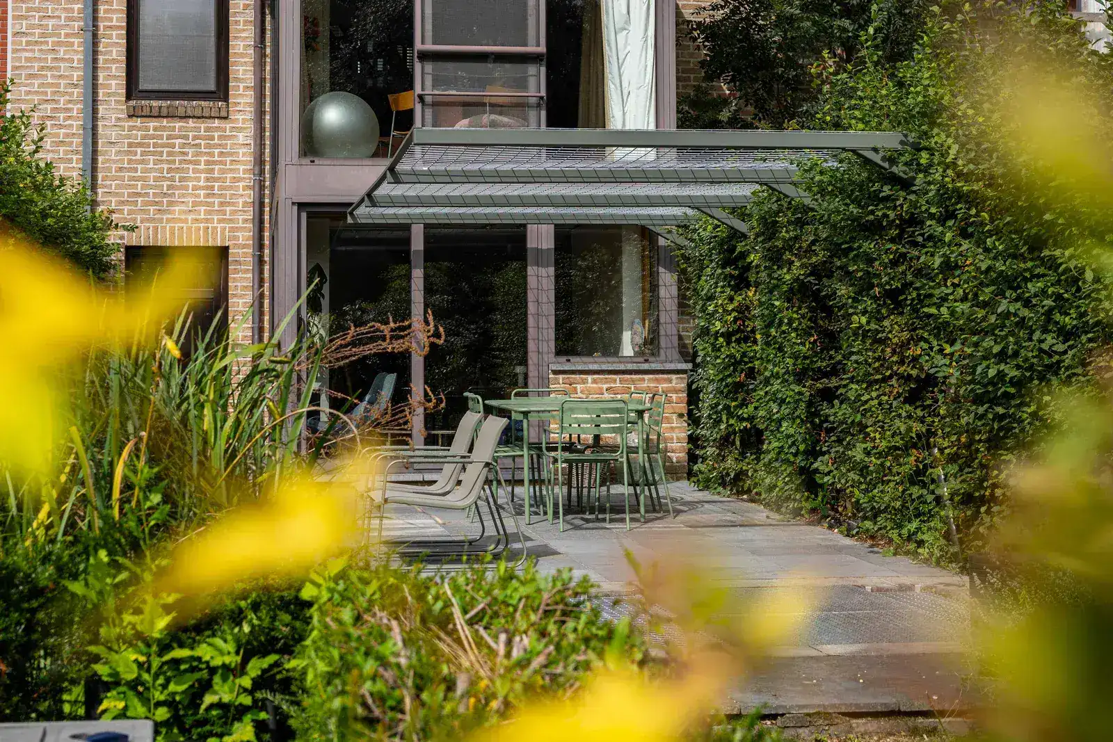 Vrijstaande stalen pergola van Staallokaal boven een terras in een groene achtertuin