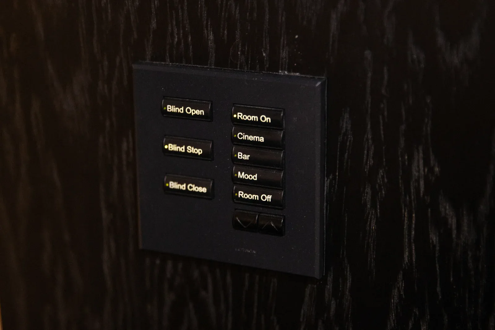 Dark wall keypad with engraved buttons for blinds open, stop, close, room on, cinema, bar, mood and room off