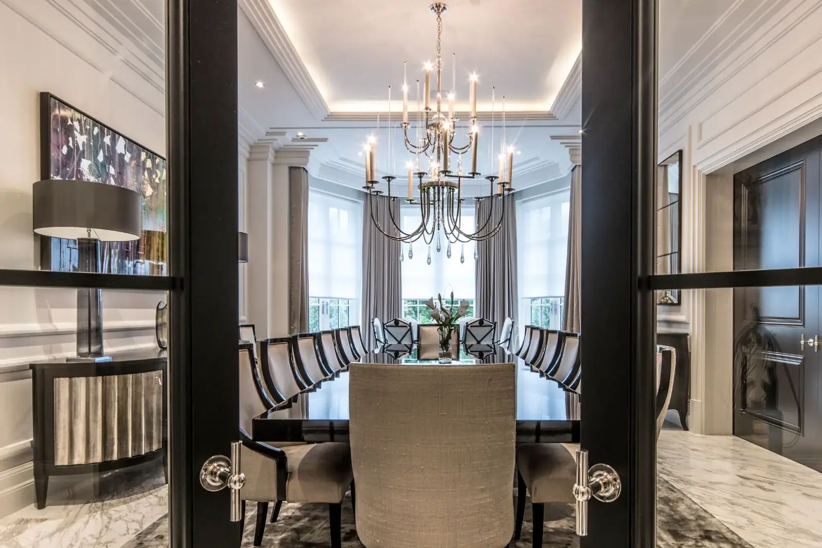 Dining room with a long table, crystal chandelier and cove lighting, seen through double doors