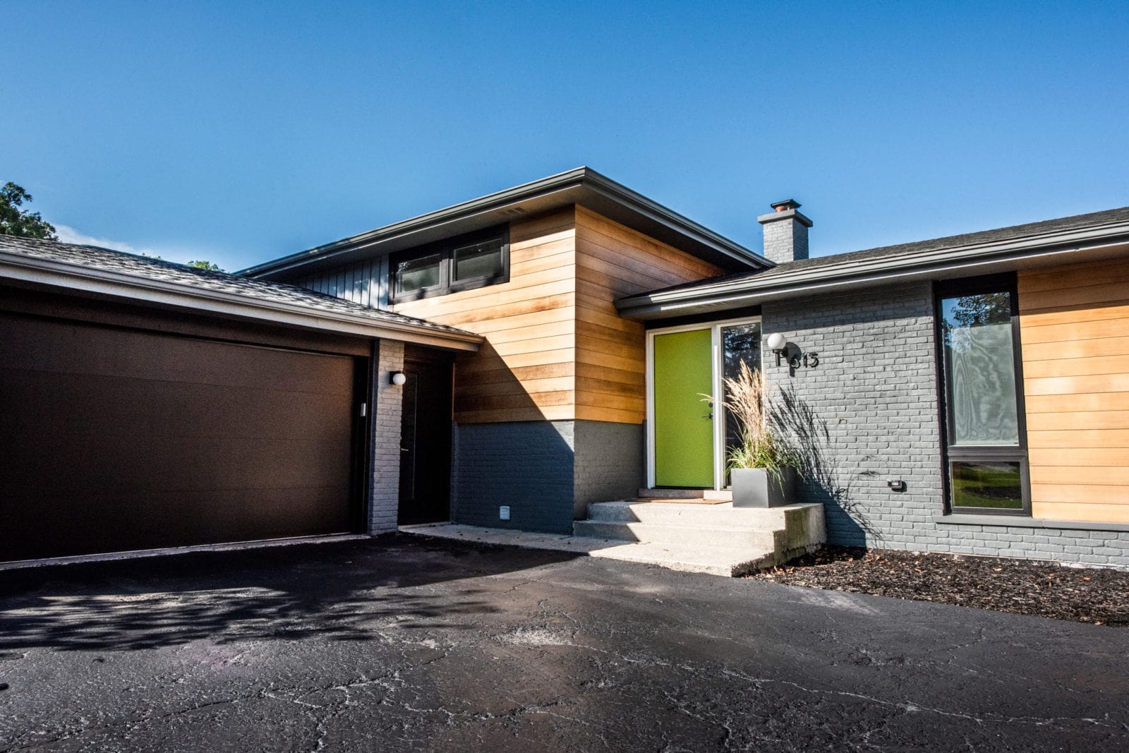 Outside of a house with grey brick and light wood board siding, black garage door & green front door
