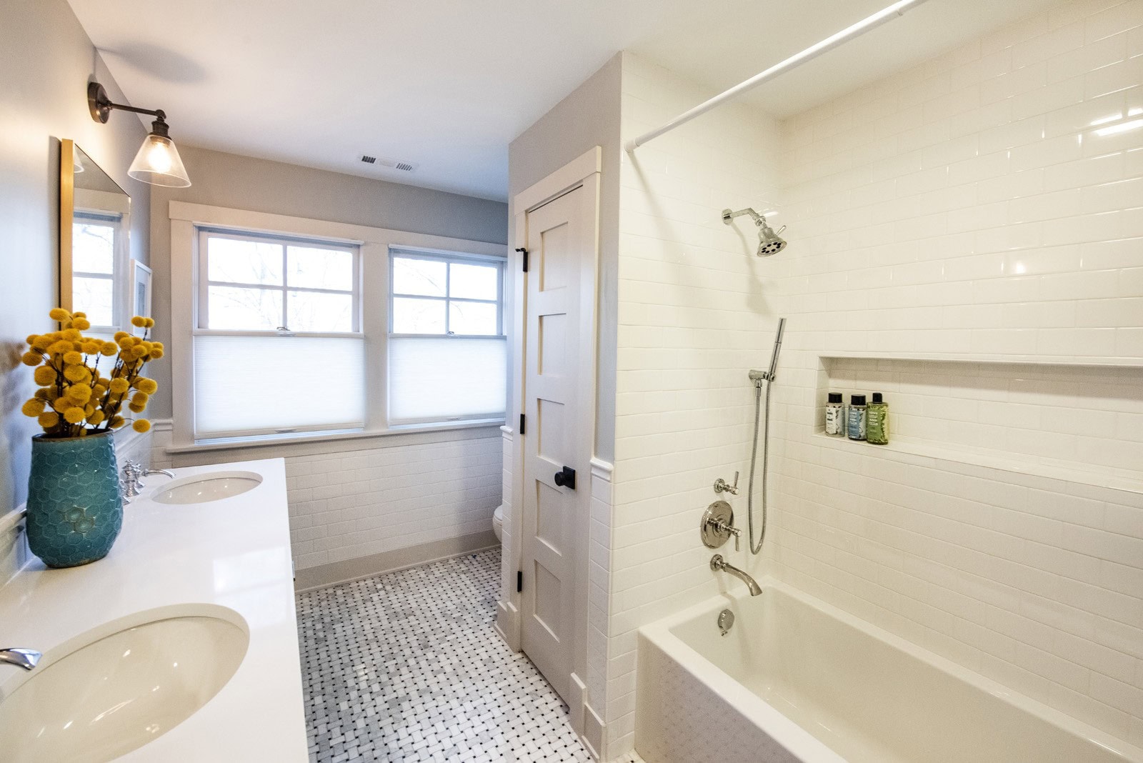 Bright white bathroom update with grey patterned tile floor & teal vase holding yellow flowers on the vanity
