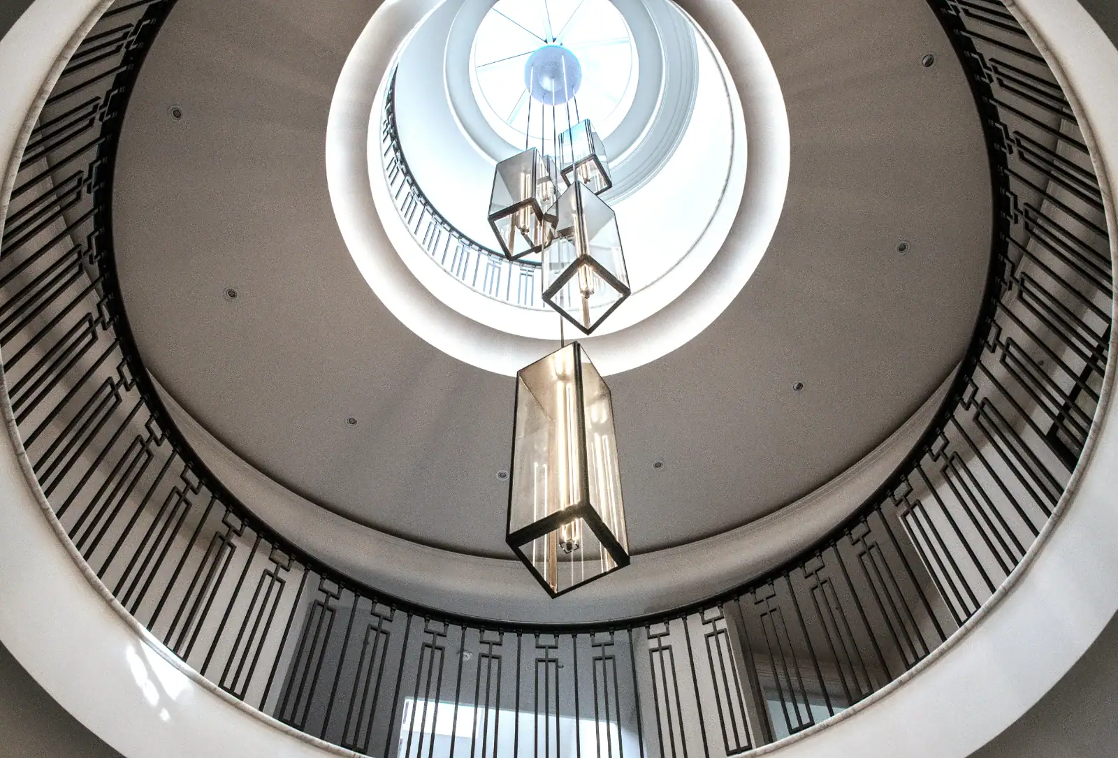 Looking up a circular staircase towards a tall geometric pendant light and a skylight