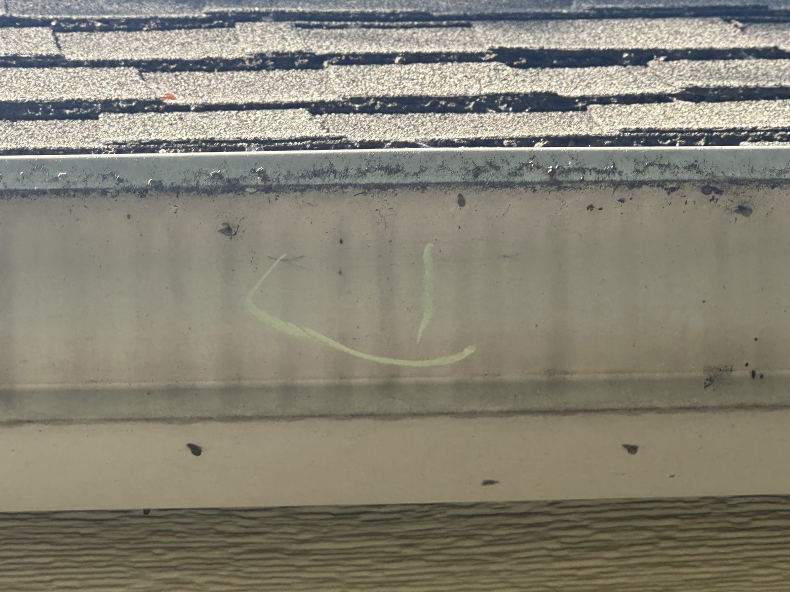 Gutter with chalk marking and dirt accumulation on shingles.