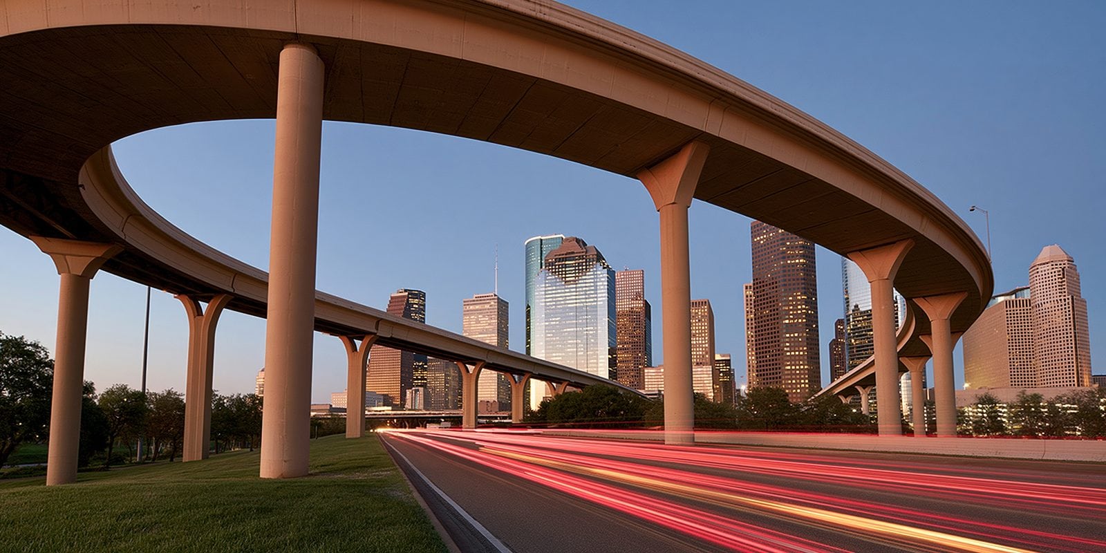 Houston freeway overpass at dusk with the downtown skyline and light trails from passing traffic