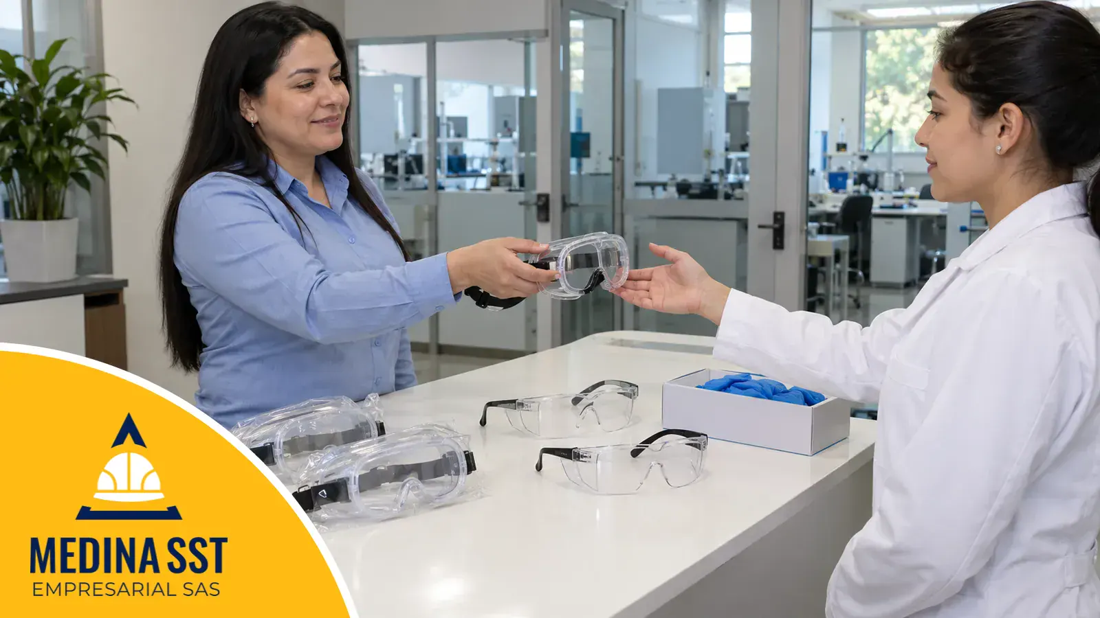 Técnica de laboratorio con bata blanca sostiene unas gafas de seguridad de laboratorio tipo monogafa nuevas, junto a otras monogafas, gafas con protección lateral y una caja de guantes de nitrilo en el mostrador de entrada