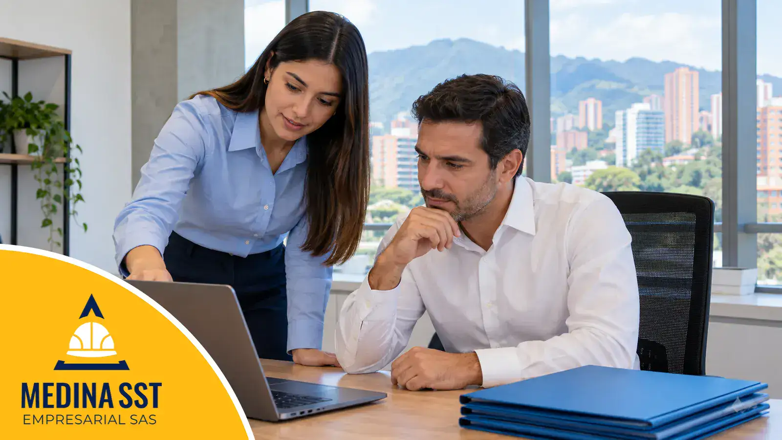 Una profesional de seguridad y salud en el trabajo revisa con el gerente de una empresa la matriz de cumplimiento legal en la pantalla de un portátil, con carpetas de evidencias sobre el escritorio