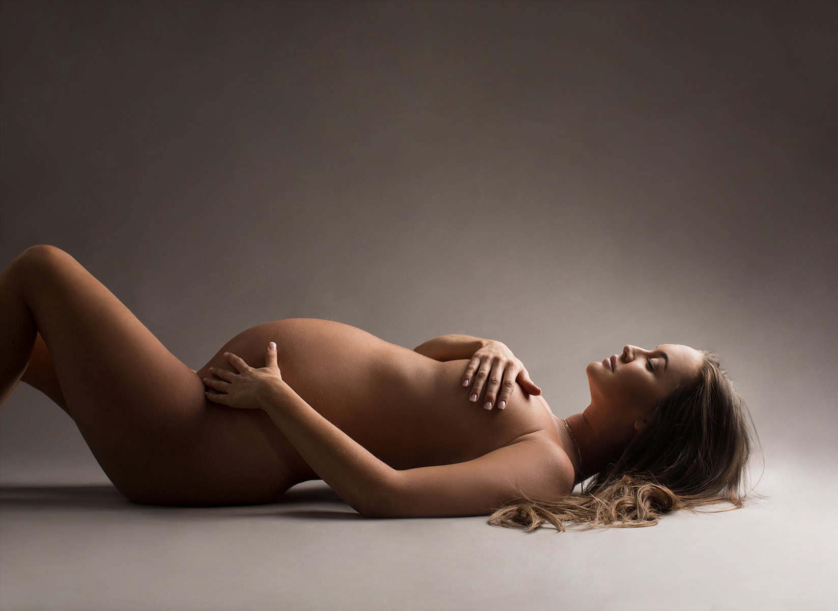 Kvinne som poserer gravid naken i studiobelysning, vekt på den skjønne mage, symbol på graviditet og morskap, perfekt for gravidfotografering.